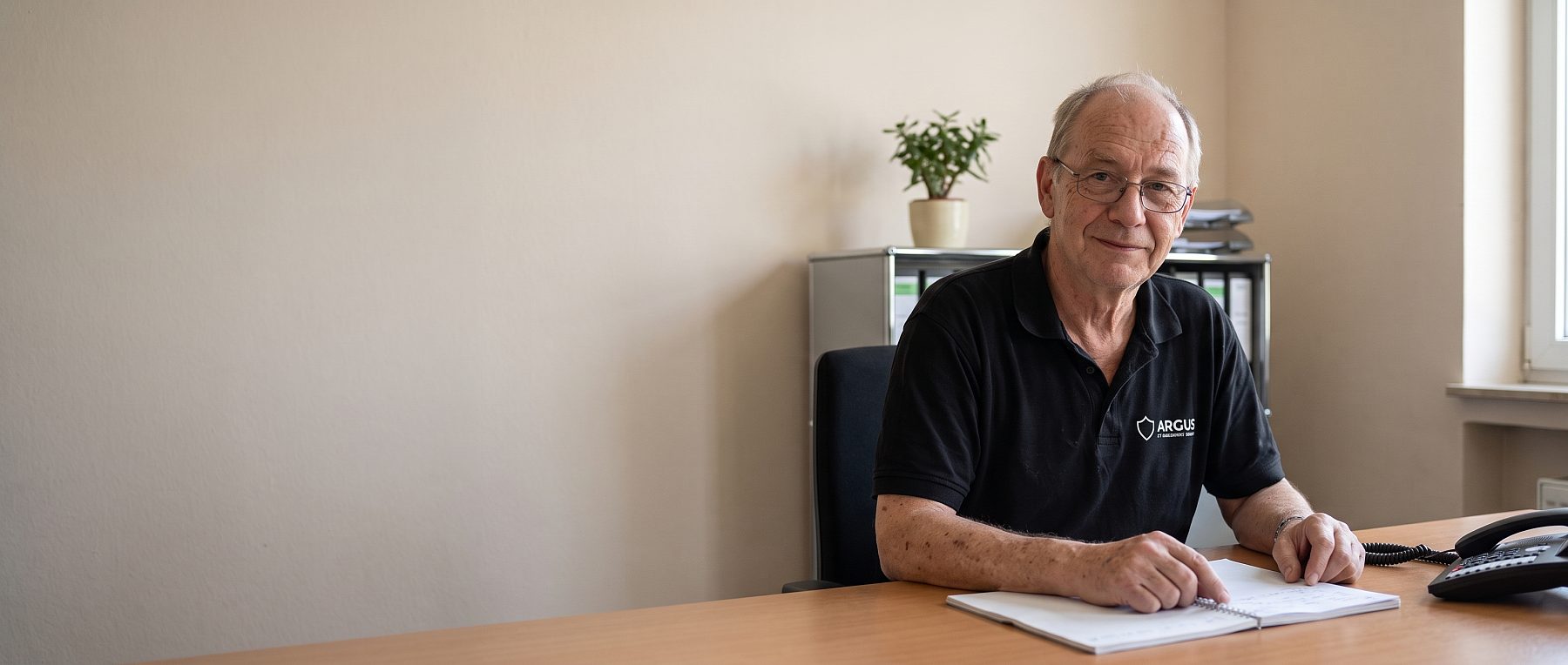 Mitarbeiter der ARGUS Sicherheit GmbH am Schreibtisch, freundlich zugewandt